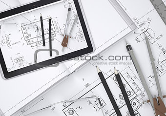 Tablet pc lying on open enpty book and engineering drawings. Tools are close by