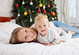 Portrait of happy mother and baby boy on bed at home with decorated Christmas tree in background