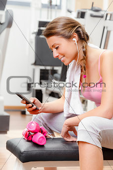 smiling woman with smartphone at the gym