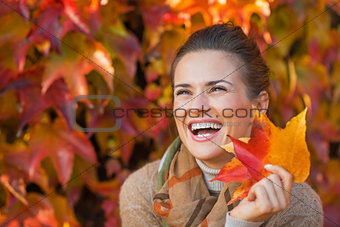 Portrait of smiling young woman with autumn leafs in front of fo
