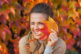 Portrait of happy young woman hiding behind autumn leafs in fron