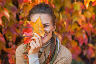 Portrait of happy young woman hiding behind autumn leafs in fron