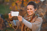 Happy young woman in autumn evening outdoors taking photo with c
