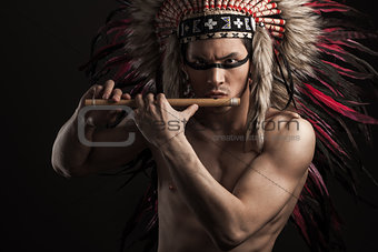 Portrait of the indian strong man posing with traditional native american make up. Playing flute