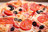 Close-up shot of Italian pizza with ham, tomatoes and olives 
