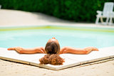 Relaxed young woman laying in pool. rear view