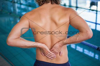 Mid section of a shirtless swimmer with back ache by pool