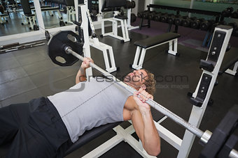Young muscular man lifting barbell in gym