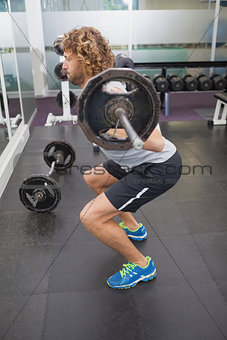 Side view of muscular man lifting barbell in gym