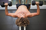 Shirtless man exercising with dumbbells in gym