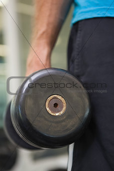 Mid section of man holding dumbbell in gym