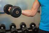Mid section of man exercising with dumbbell in gym