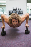 Handsome man doing push ups with kettle bells in gym