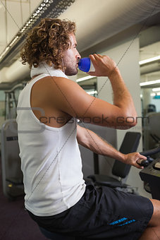 Side view of man drinking water on exercise bike at gym