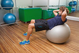 Man doing abdominal crunches on fitness ball in gym