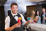 Handsome barman smiling at camera holding cocktails