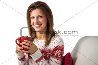 Smiling cute brunette holding cup of coffee sitting on sofa