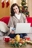Smiling brunette shopping online with laptop at christmas