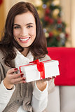 Smiling brunette holding gift on the couch at christmas