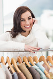 Beauty brunette smiling at camera by clothes rail