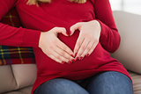 Close up of a pregnant woman doing heart sign on her belly