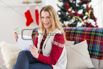 Cute blonde sitting on couch holding credit card and tablet