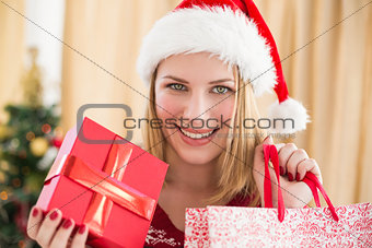 Festive blonde showing a gift while looking at camera