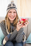 Happy blonde in winter hat sitting on couch showing a gift