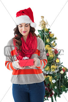 Festive brunette holding gift by the tree