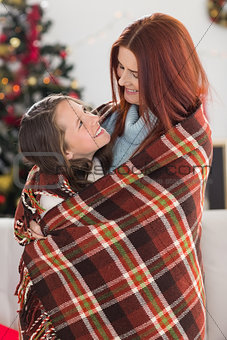 Festive mother and daughter wrapped in blanket