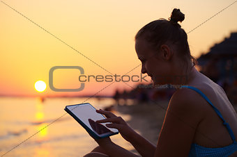 Smiling woman using pad on beach at sunset