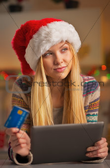 Portrait of thoughtful teenager girl in santa hat with credit ca