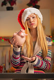 Portrait of displeased teenager girl in santa hat with piggy ban