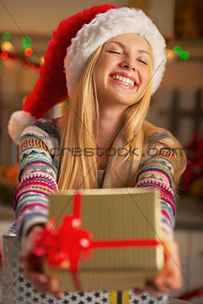 Happy teenager girl in santa hat giving christmas present box