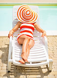 Young woman laying on sunbed with hat on head
