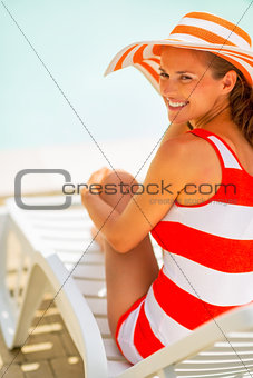 Smiling young woman in hat sitting on sunbed
