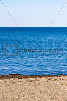 Small beach on blue water on white sky