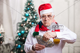 Senior man in Santa's hat holding money on Christmas background