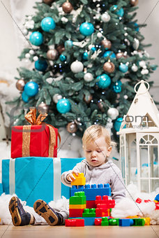 Cute toddler boy playing with building blocks at Christmas tree