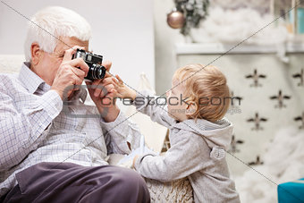 Senior man taking photo of his toddler grandson at Christmas time