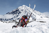 Backpack, skis and poles lie on the snow on background volcano