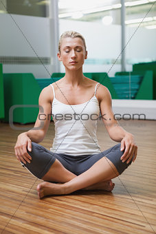 Sporty woman sitting with eyes closed in fitness studio