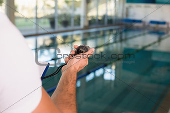 Cropped swimming coach with stopwatch by pool at leisure center