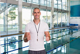 Swimming coach gesturing thumbs up by pool at leisure center