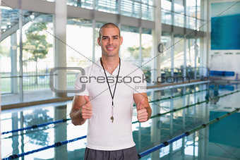 Swimming coach gesturing thumbs up by pool at leisure center
