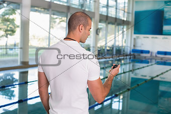 Swimming coach looking at stopwatch by pool at leisure center