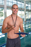 Shirtless coach with stopwatch by pool at leisure center