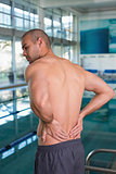 Rear view of shirtless swimmer with back ache by pool