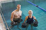 Swimmers working out with foam dumbbells in swimming pool at leisure centre