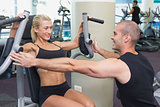 Trainer assisting woman on fitness machine at gym